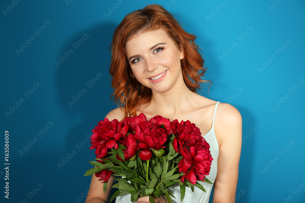 Happy young woman holding beautiful peony flowers on color background
