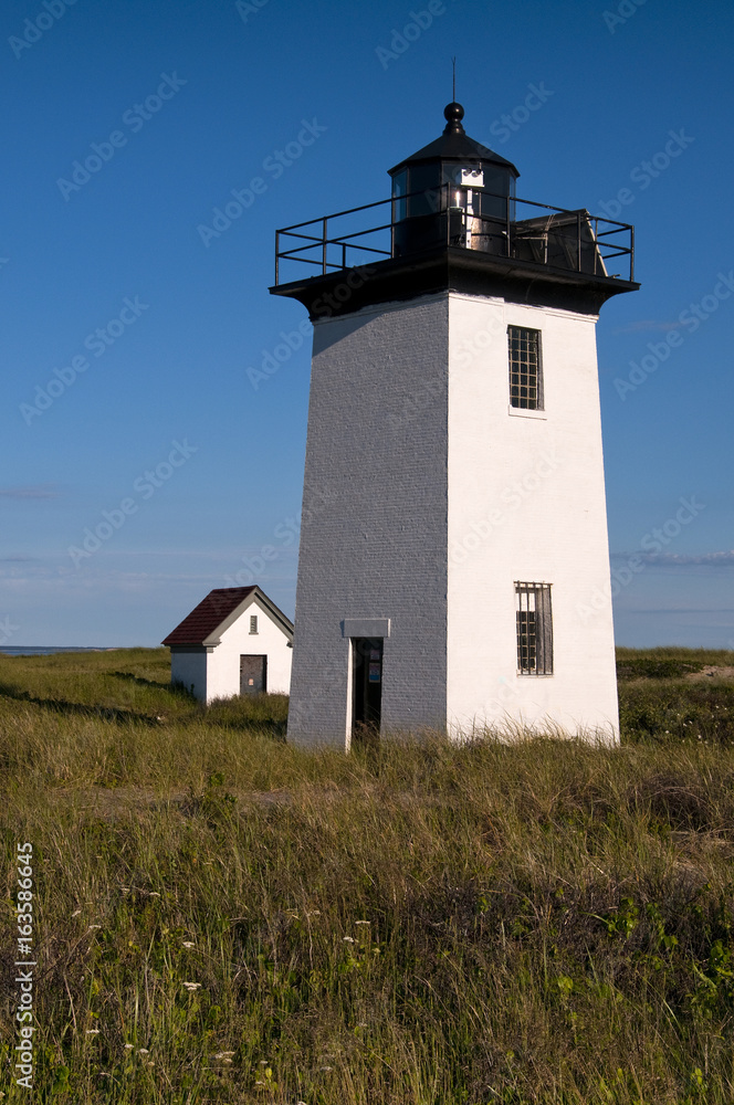 Sunlit lighthouse tower with oil house outside of Provincetown on Cape Cod on a summer late afternoon.