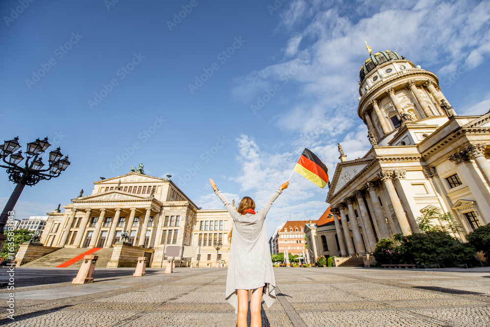 Fototapeta premium Young woman tourist standing back with german flag on the Gendarmen square with French church and Opera house on the background in Berlin
