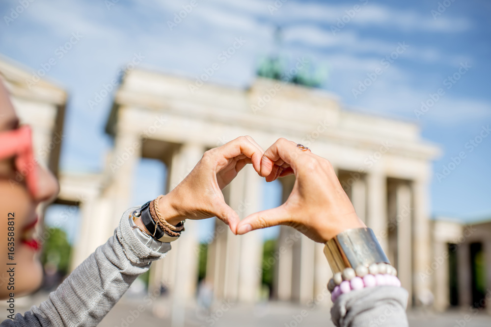 Fototapeta premium Młoda kobieta turystyczny kształt serca z rękami przed słynnymi bramami Brandenburgii w Berlinie