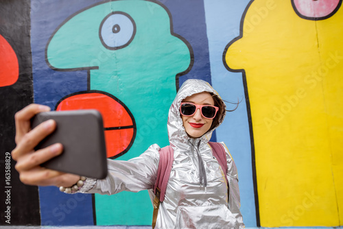 Young woman tourist making selfie photo standing in front of the Berlin wall in Germany