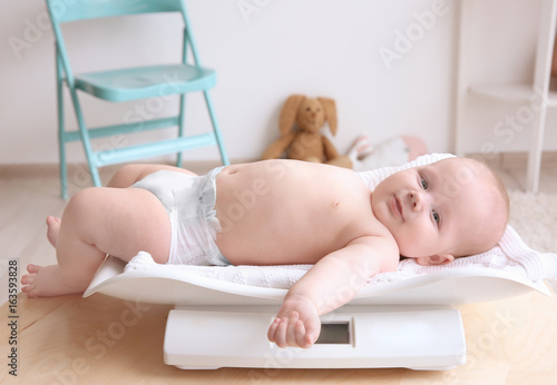Baby lying on scales in room