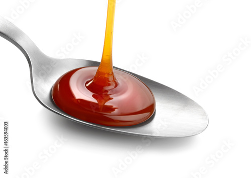 Tasty caramel sauce pouring into spoon on white background