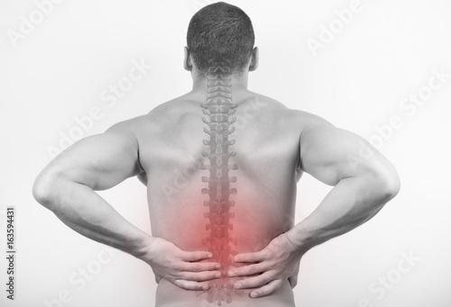 Rear view of a young man holding his back in pain, isolated on white background. Lower back pain. Shirtless man touching his back for the pain. 