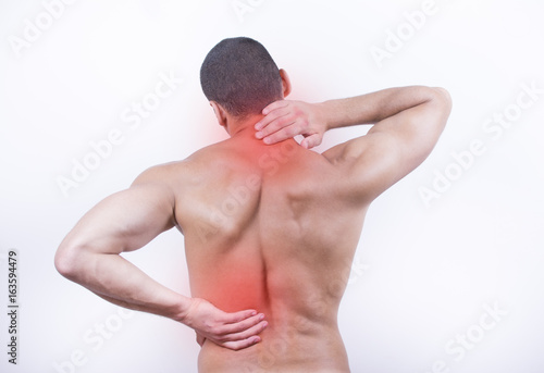 Rear view of a young man holding his neck and back in pain, isolated on white background. Lower back pain. Shirtless man touching his neck and back for the pain.
