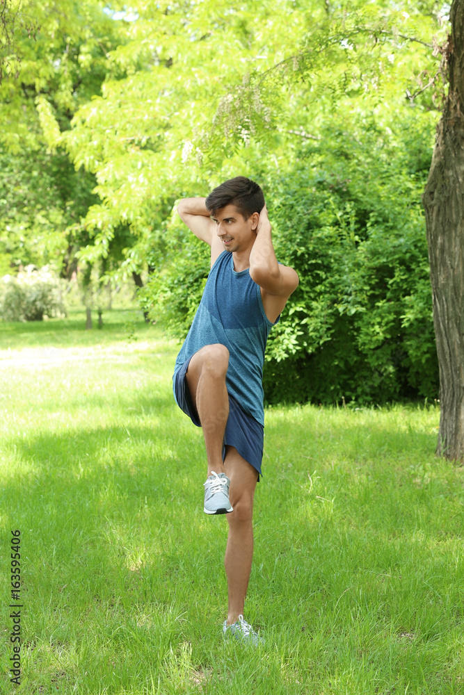 Athletic young man doing bicycle crunch exercise while standing on grass in green spring park Athletic young man doing bicycle crunch exercise while standing on grass in green spring park