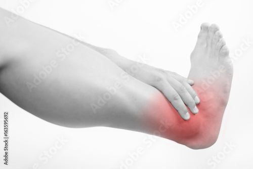 Close up view of a young man holding his ankle in pain, isolated on white background. Lower leg pain. Young man touching his ankle for the pain. Red inflammation effect. © Addoro