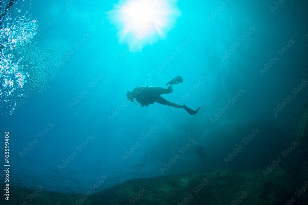 Scuba Divers, silhouettes against sunburst, in the ocean beside coral reef