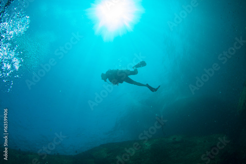 Scuba Divers, silhouettes against sunburst, in the ocean beside coral reef