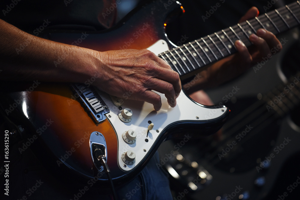 Fototapeta premium Man's hands playing on an electric guitar in a band on stage, entertainment of a guitarist artist with his music instrument