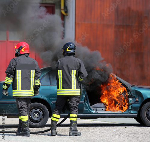 incident car with flames and black smoke and two firefighters