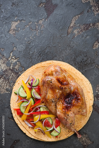 Tortillas with roasted halved chicken and fresh vegetables, flat-lay with copyspace on a brown stone surface, vertical shot