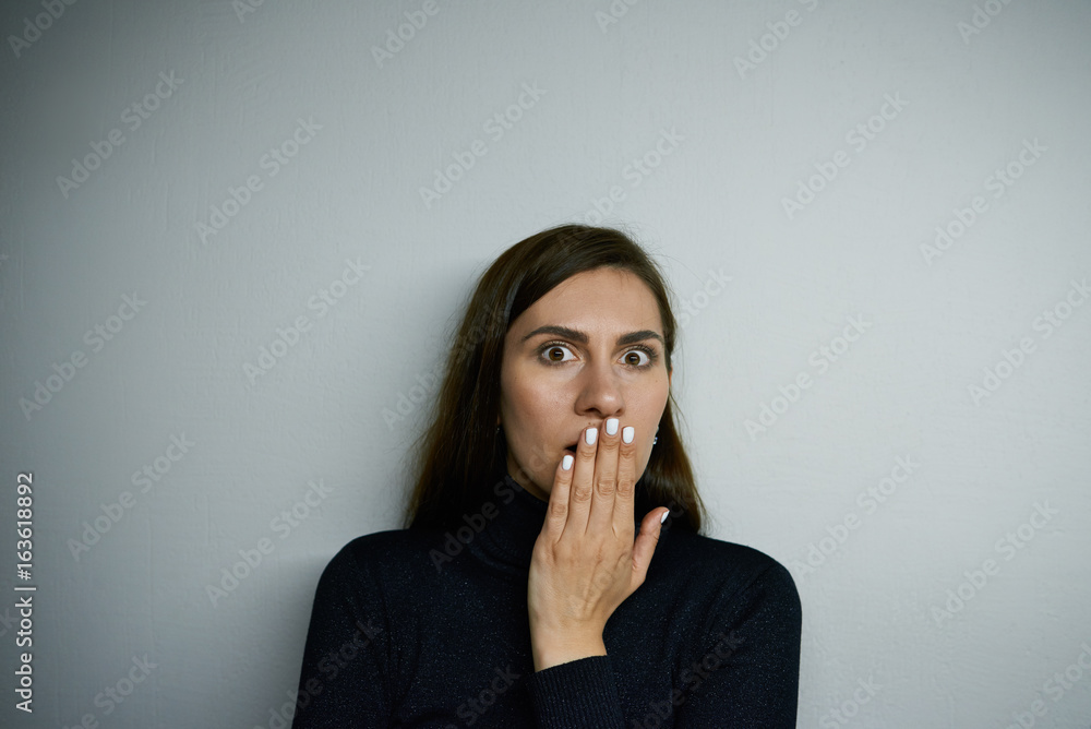 Brunette woman covering mouth with hand and looking at camera with astonishment, shocked with unbelievable unexpected news. Studio shot of surprised young female having stunned expression on her face Brunette woman covering mouth with hand and looking at camera with astonishment, shocked with unbelievable unexpected news. Studio shot of surprised young female having stunned expression on her face