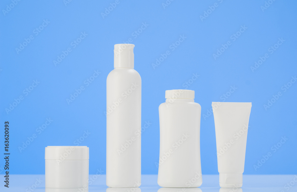 Set of tubes and containers of cream or gel in white plastic packaging. Product mockup with mirror reflection on white table with blue background. Set of tubes and containers of cream or gel in white plastic packaging. Product mockup with mirror reflection on white table with blue background.