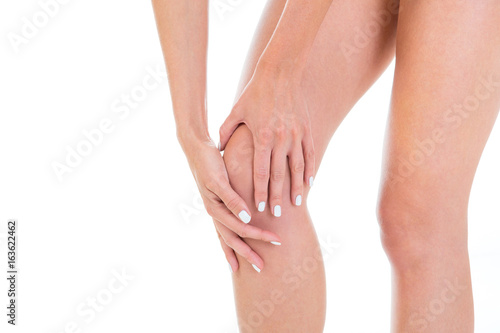 Fototapeta Naklejka Na Ścianę i Meble -  Gorgeous girl model demonstrates her knee. Close-up of beautiful woman with hands on her knee isolated on white background