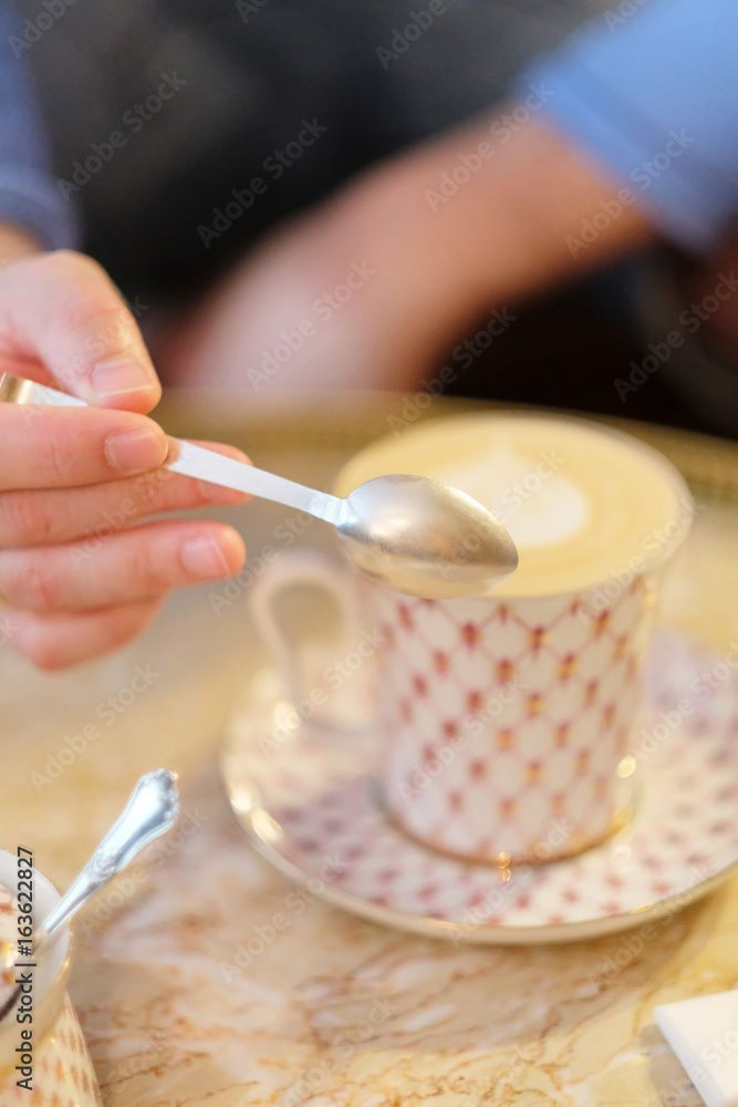 Hand of a young man with a spoon over a cup of coffee cappuccino on a table in a cafe