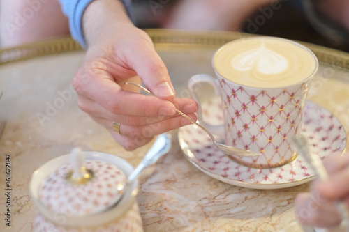 Hand of a young man with a spoon over a cup of coffee cappuccino on a table in a cafe