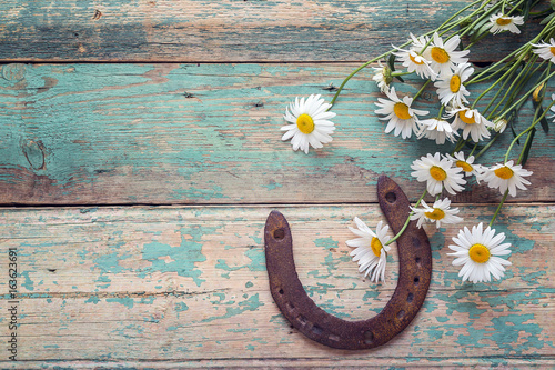 Rustic background with rusty horseshoe and bouquet of daisies on old wooden boards. Copy space.