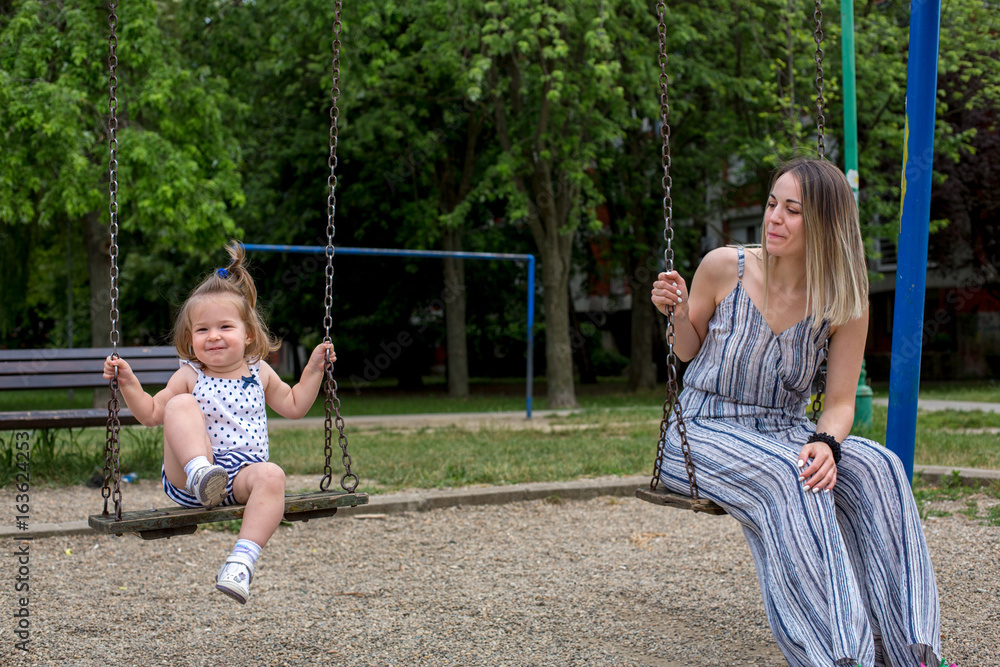 Mother and daughter at playground swinging.