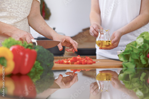 Close-up of four human hands are cooking in a kitchen. Friends having fun while preparing fresh salad. Vegetarian, healthy meal and friendship concept