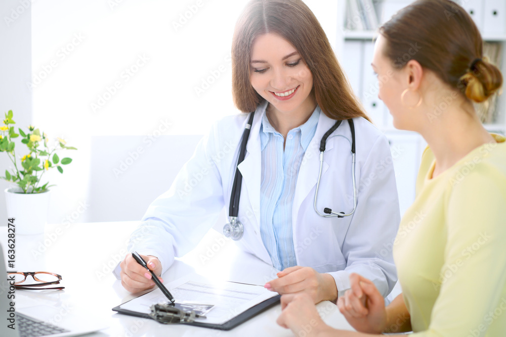 Doctor and patient have a talk while sitting at the desk near window Doctor and patient have a talk while sitting at the desk near window