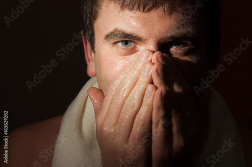 A man is washing himself after a heavy workout in the twilight in a ray of light