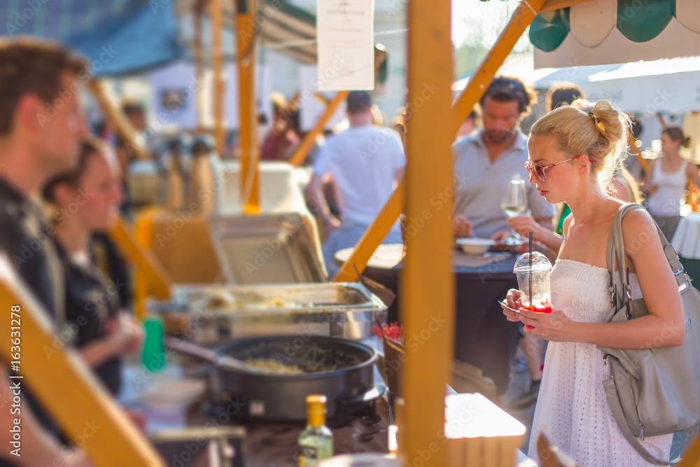 Φωτογραφία Beautiful blonde caucasian lady wearing white summer dress buying freshly prepared meal at a local street food festival