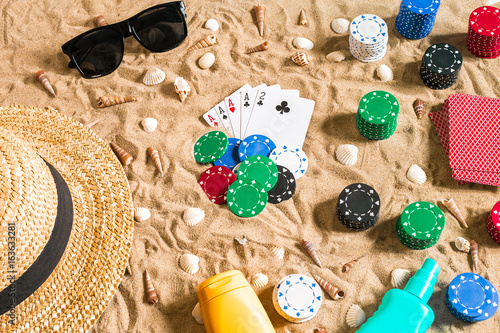 Beachpoker. Chips and cards on the sand. Around the seashells, sunglasses and hat. Top view