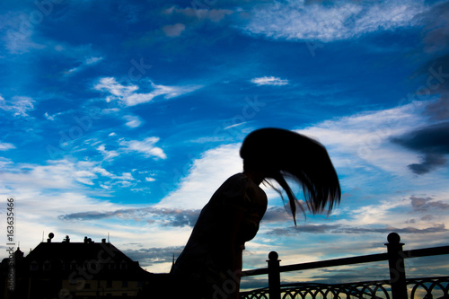 Silhouette of a girl against a blue sky playing with her hair © andriushchenko