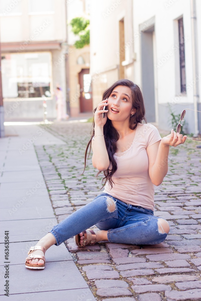 Young beautiful woman brunette walks at the city in Europe. Summer. Happy girl. Street fashion. Young beautiful woman speaks by phone. The girl takes pictures of herself.