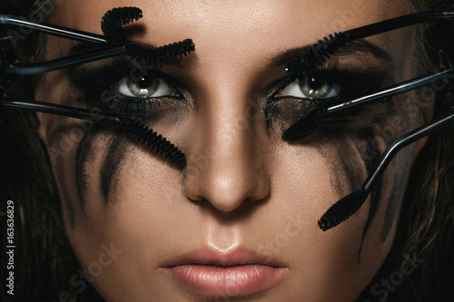 Woman with smudges of makeup on her face and broken mascara brushes photo