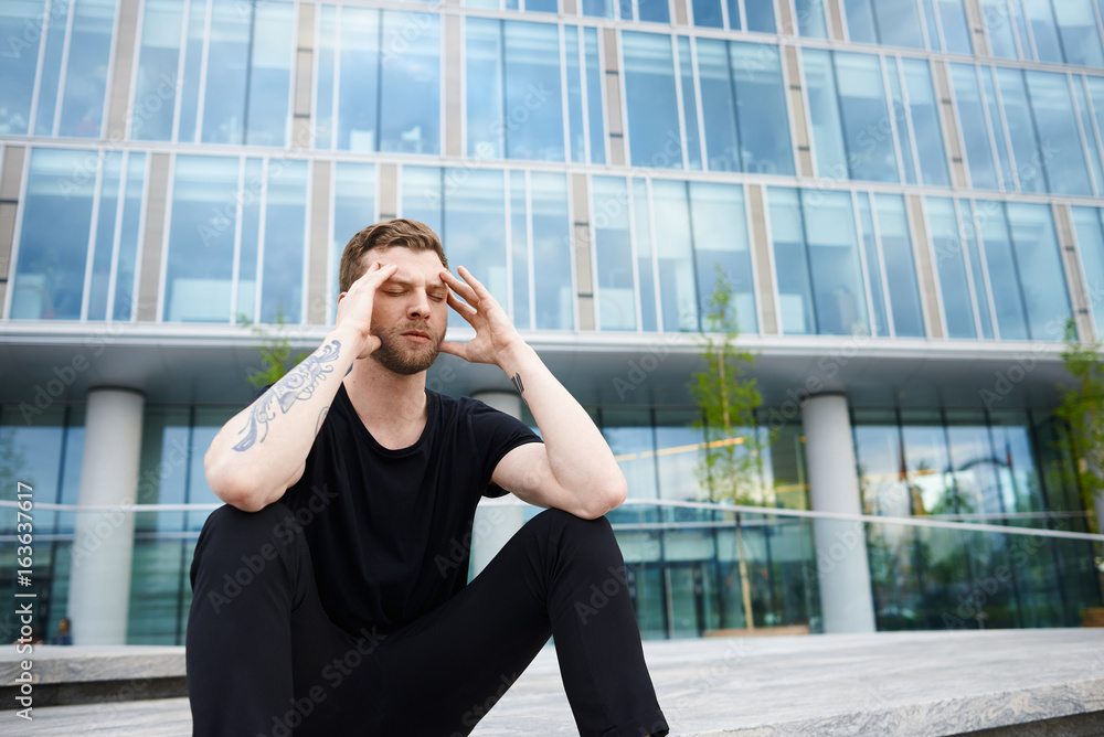 Depression concept of office manager. Stylish man sitting on steps and hold head by two hands. Guy have relax and planning new real business project after resolving problems. Male in black. Depression concept of office manager. Stylish man sitting on steps and hold head by two hands. Guy have relax and planning new real business project after resolving problems. Male in black.