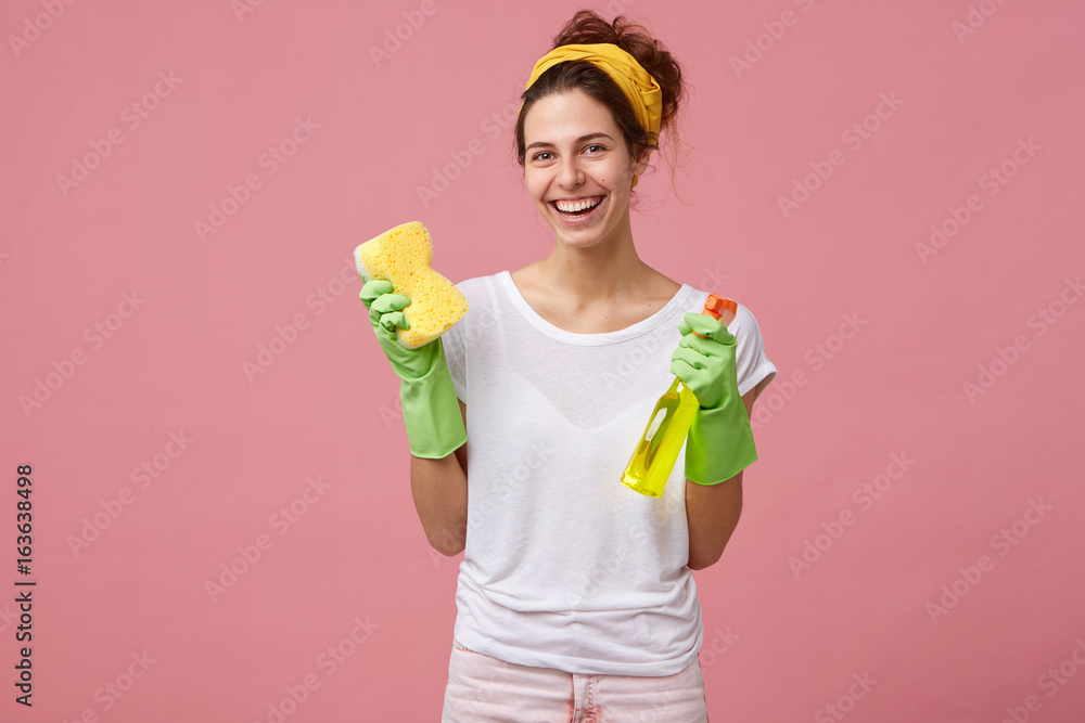 Φωτογραφία Portrait of happy female doing house duties wearing rubber gloves and holding detergent with sponge having good mood