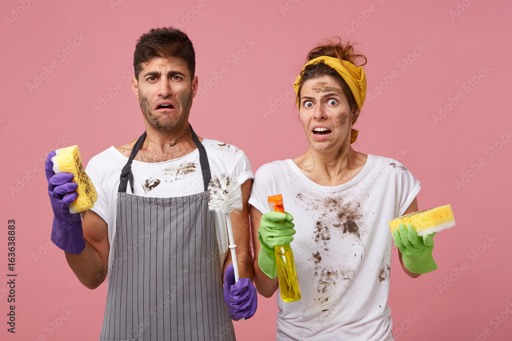 Φωτογραφία Young family couple with dirty faces having disgusting look holding window cleaner and sponges washing windows in living room