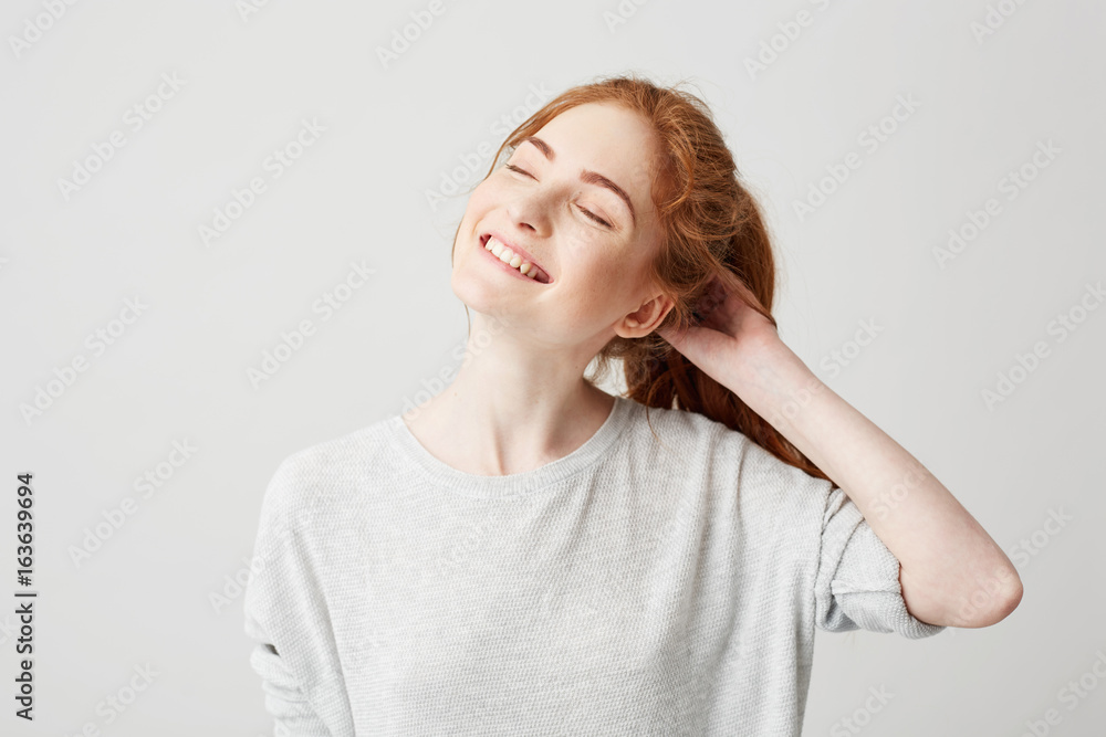 Φωτογραφία Portrait of happy young cute redhead girl smiling with closed eyes touching hair over white background