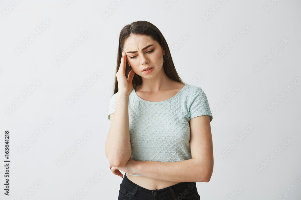 Young beautiful brunette girl frowning touching temple with hand. Headache. Isolated on white background.
