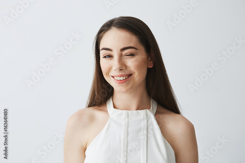 Portrait of young beautiful tender girl in blouse looking at camera winking smiling over white background.