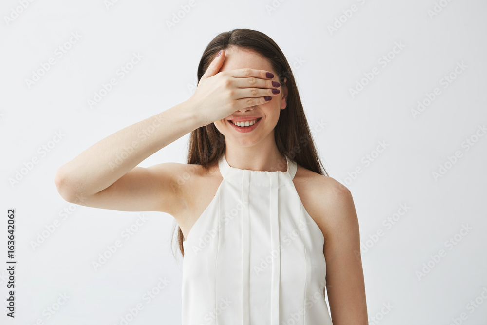 Portrait of young brunette girl covering eyes with hand smiling over white background. Portrait of young brunette girl covering eyes with hand smiling over white background.
