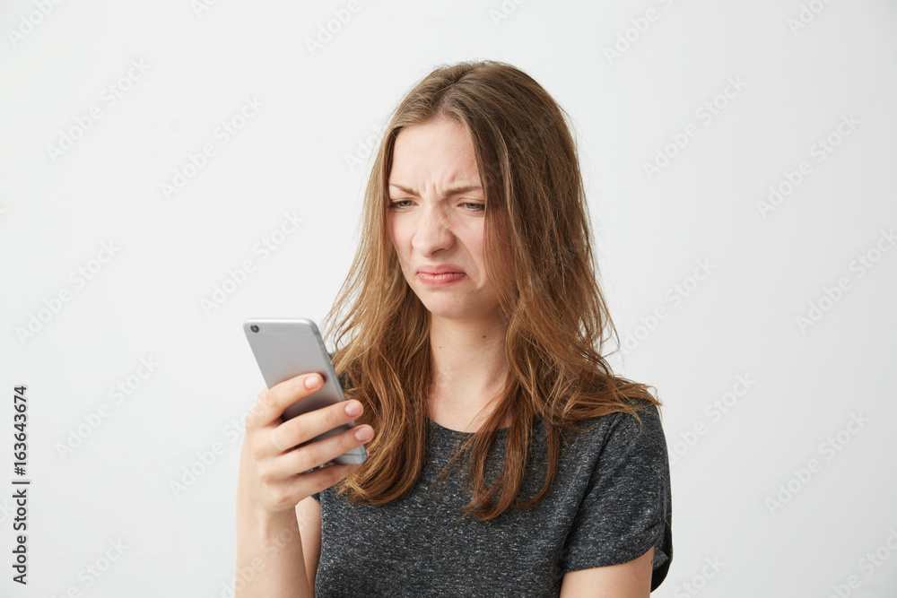Displeased dissatisfied young girl looking at phone screen over white background. Displeased dissatisfied young girl looking at phone screen over white background.