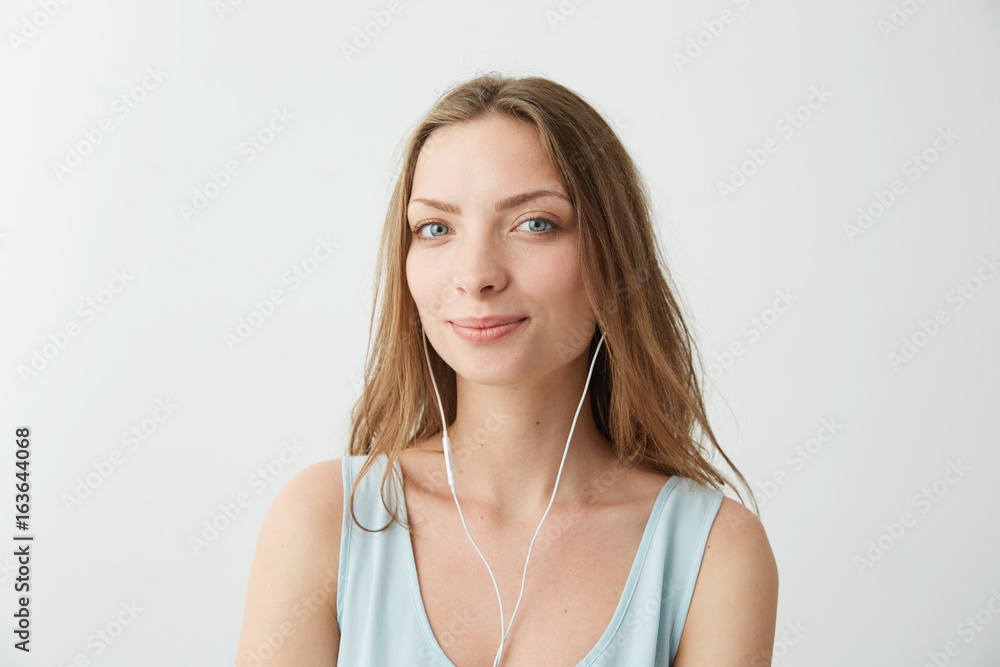 Tender dreamy young pretty girl looking at camera listening to streaming music in headphones over white background. Tender dreamy young pretty girl looking at camera listening to streaming music in headphones over white background.