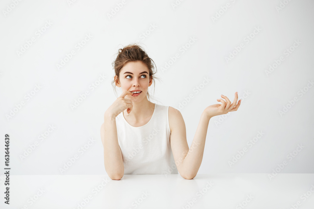 Dreamy beautiful young girl with bun sitting at table over white background thinking dreaming. Dreamy beautiful young girl with bun sitting at table over white background thinking dreaming.