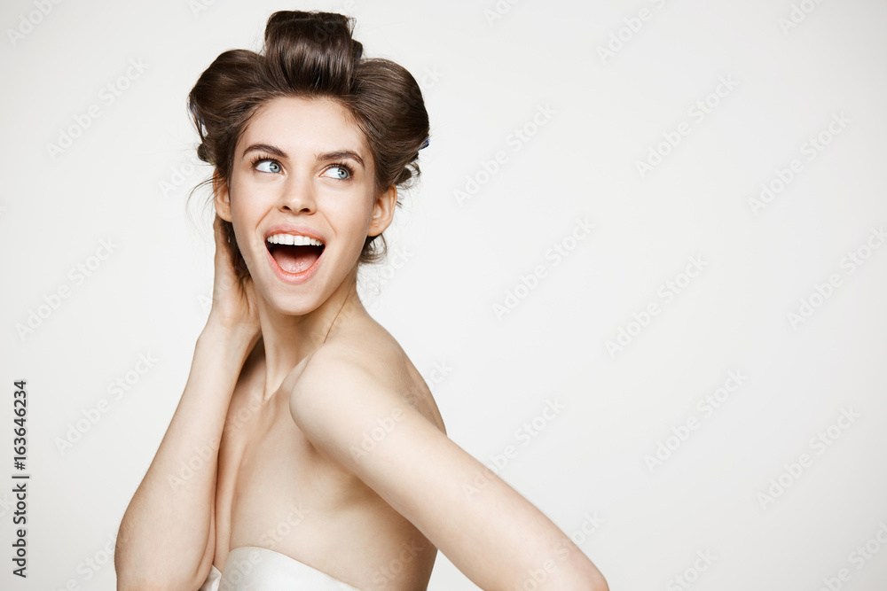 Surprised young beautiful girl in hair curlers smiling with opened mouth over white background. Beauty and spa concept. Surprised young beautiful girl in hair curlers smiling with opened mouth over white background. Beauty and spa concept.