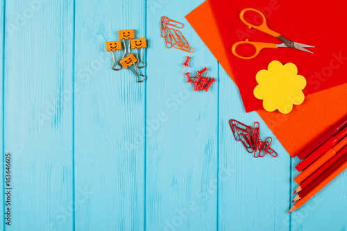 Red and orange pencils, felt-tip pens, notepaper, paper clips, stationery nails, felt and scissors on blue wooden background