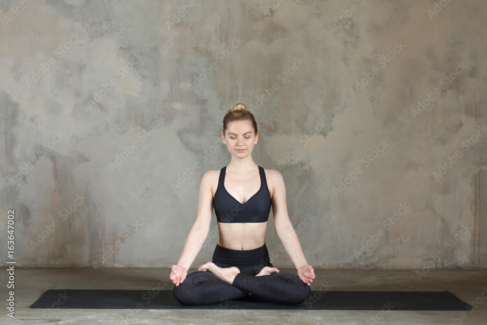 Young woman practicing Lotus pose / padmasana against texturized wall / urban background Young woman practicing Lotus pose / padmasana against texturized wall / urban background
