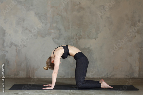 Young woman practicing cat pose / Marjariasana against texturized wall / urban background