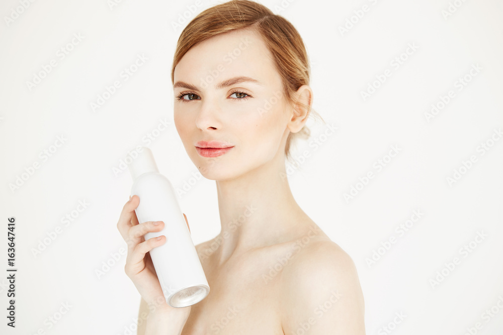 Nude beautiful blonde girl with fresh perfect skin smiling looking at camera holding cosmetology spray bottle over white background. Nude beautiful blonde girl with fresh perfect skin smiling looking at camera holding cosmetology spray bottle over white background.