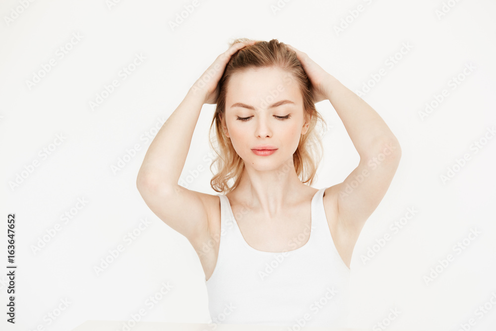 Beautiful blonde girl with clean fresh skin sitting at table over white background touching hair. Skincare beauty and spa. Closed eyes. Beautiful blonde girl with clean fresh skin sitting at table over white background touching hair. Skincare beauty and spa. Closed eyes.