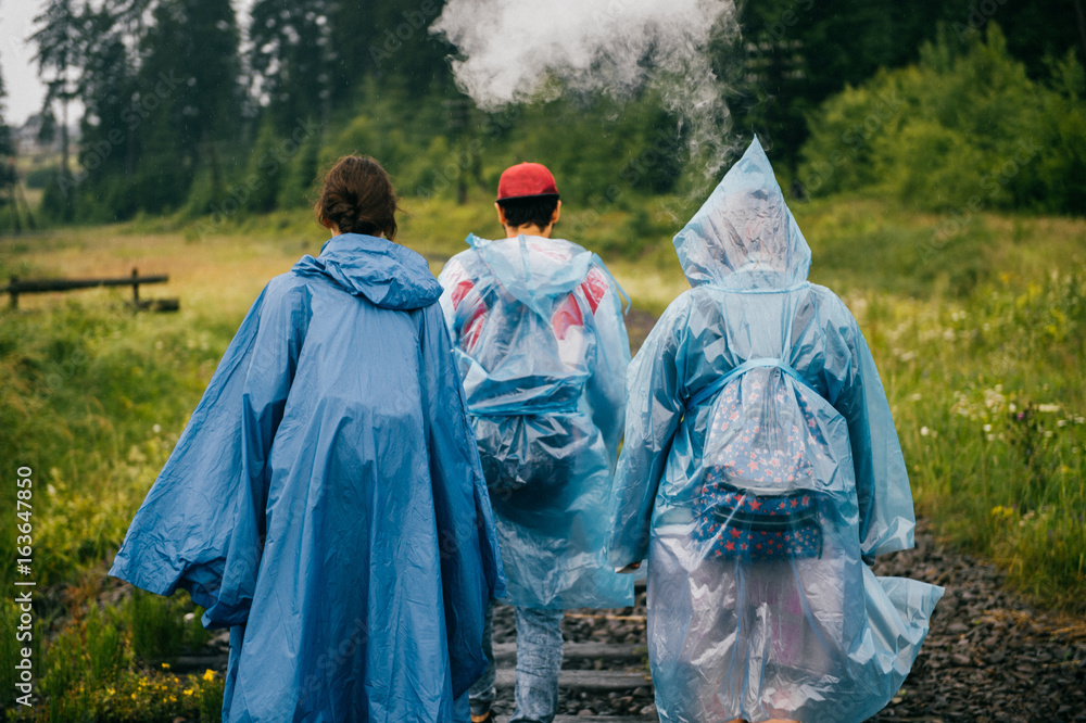 Smoking man and two women. Rebel travelers in raincoats walking in danger zone on railroad outdoor at narure. Occurrence on road. Warning. Accident. Company of friends on vacation. Tourist clothes.