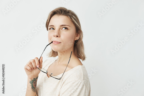 Portrait of young pretty girl smiling thinking dreaming biting glasses over white background.