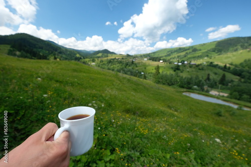 Hand with a white cup of coffee against the background of the mountains